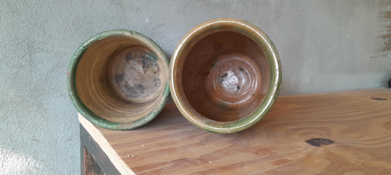 May include: Two empty, weathered ceramic pots with a green rim and a brown interior. The pots are sitting on a wooden surface. The pots are likely for plants.