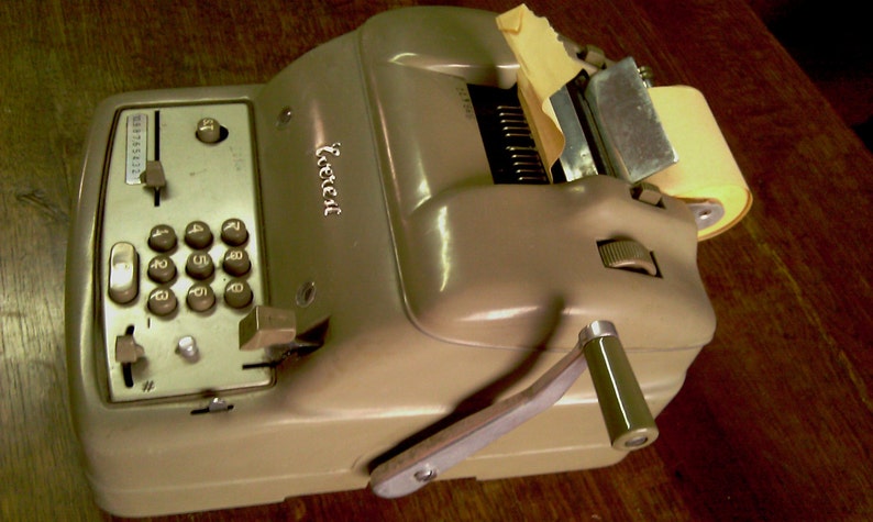 Puede incluir: Una m&aacute;quina de sumar vintage de color beige con un rollo de papel y una palanca en el lateral. La m&aacute;quina tiene un teclado num&eacute;rico y una ventana de visualizaci&oacute;n. El nombre de la marca "Facit" est&aacute; impreso en la m&aacute;quina.