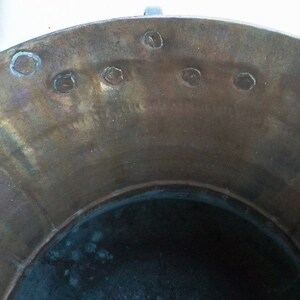 Puede incluir: La parte superior de una olla grande, redonda y de cobre con un interior oscuro. La olla tiene una serie de peque&ntilde;os agujeros redondos alrededor del borde.