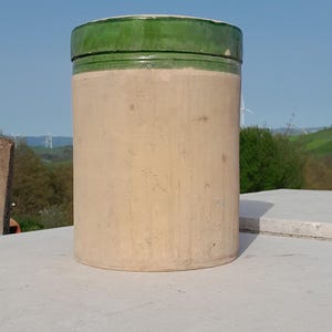 Może przedstawiać: Cylindryczny ceramiczny dzbanek z zieloną glazurą na górze i beżowym korpusem. Dzbanek stoi na białej powierzchni.
