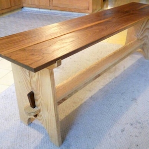 May include: A wooden bench with a walnut top and a light wood base. The bench has a simple design with a single shelf.