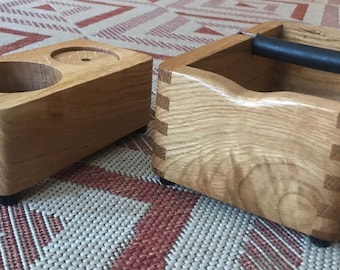 May include: Two wooden coffee accessories. A light brown wooden stand with two cup holders and a small hole in the center. A light brown wooden box with a black handle and a small hole in the center.