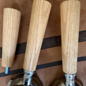 May include: Three wooden handles for espresso portafilters. The handles are made of light brown wood with a grain pattern. The handles are attached to silver metal portafilters.