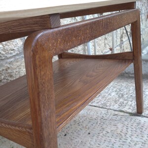 May include: A wooden coffee table with a lower shelf. The table has a light brown top and dark brown legs and shelf. The table is made of solid wood and has a natural finish.