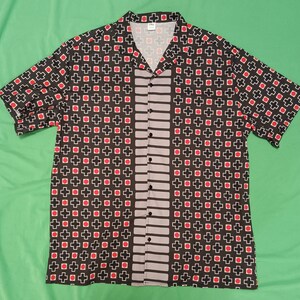 May include: A black and white short-sleeved button-up shirt with a red and white geometric pattern. The shirt has a vertical stripe pattern down the center.
