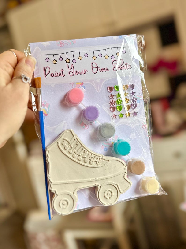 Puede incluir: Un kit de patines de ruedas para pintar en una bolsa de pl&aacute;stico transparente. El kit incluye un pat&iacute;n de ruedas, botes de pintura de varios colores, un pincel y gemas decorativas. El texto "Paint Your Own Create".