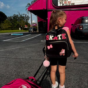 Könnte beinhalten: Ein junger Mensch mit einem schwarzen Rucksack mit dem Wort "SKATE" in Rosa und einer Rollschuhgrafik. Die Person zieht eine rosa Rollentasche mit einem weißen Logo. Im Hintergrund ein rosa Gebäude mit der Aufschrift "OPEN SKATE".