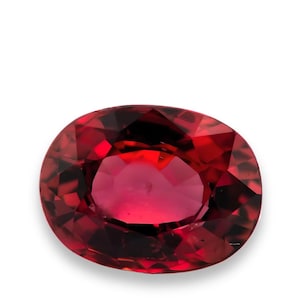 May include: A faceted, oval-shaped, red gemstone. The gem has a deep, rich colour with internal reflections, and is set against a white background. The cut of the stone creates multiple facets that reflect light.