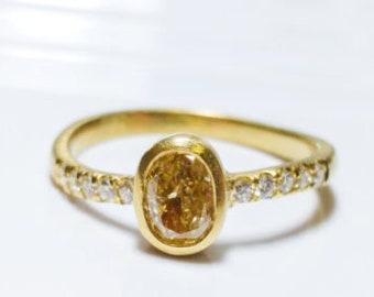 Puede incluir: Un anillo de oro con una piedra preciosa ovalada amarilla rodeada de diamantes más pequeños.