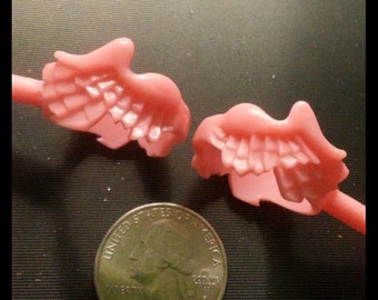 May include: Two pink plastic angel wings with a feathery design. The wings are attached to a stick.