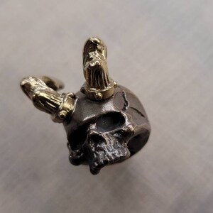 May include: A small, detailed skull charm with gold horns. The skull is made of metal and has a dark, aged finish.