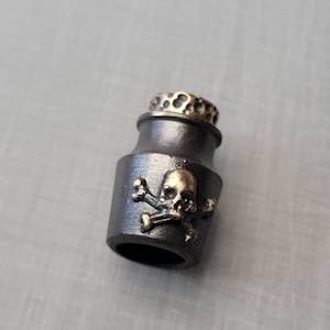 May include: A black metal bottle stopper with a gold skull and crossbones design.