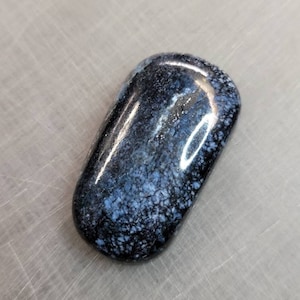 May include: A smooth, dark blue and white stone with a speckled pattern. The stone is polished and has a glossy finish.