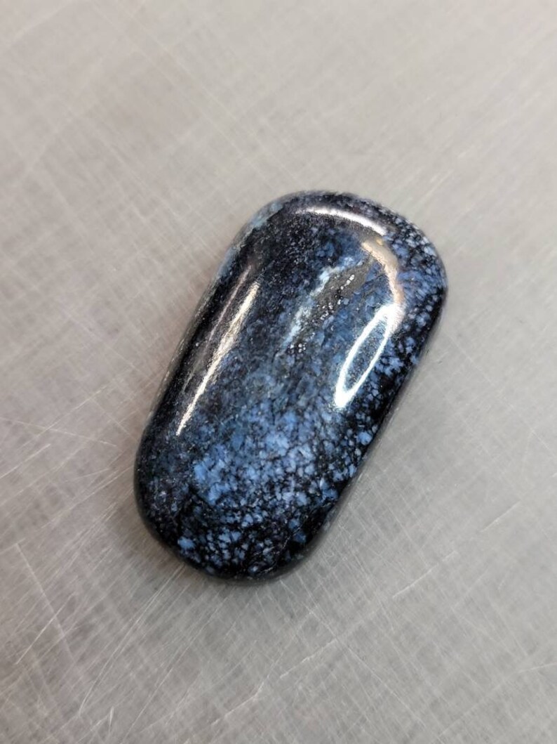 May include: A smooth, dark blue and white stone with a speckled pattern. The stone is polished and has a glossy finish.