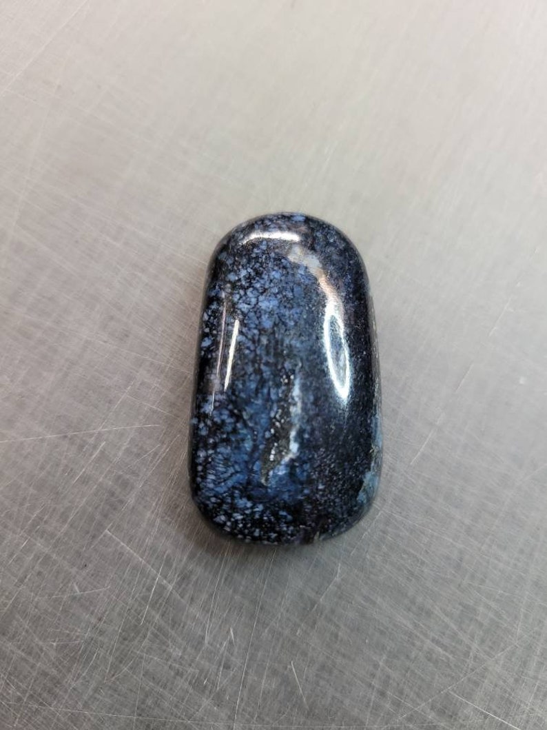 May include: A smooth, polished, dark blue and white stone with a mottled pattern. The stone is oval shaped and has a glossy finish.