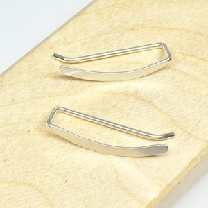 May include: A pair of silver ear cuffs. The cuffs are curved and have a simple, minimalist design.