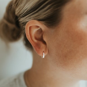 Op de afbeelding: Een close-up van een oor met een kleine, zilveren oorring.