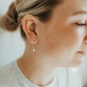 Puede incluir: Primer plano de la oreja de una persona con un fino aro de oro. El arete es un diseño simple y minimalista.