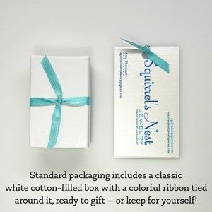 Puede incluir: Una caja blanca con una cinta azul claro atada alrededor. La caja est&aacute; sobre una superficie blanca. Tambi&eacute;n se muestra una tarjeta de presentaci&oacute;n de Squirrel's Nest Jewelry. La tarjeta es blanca con texto azul y dice "Squirrel's Nest Jewelry Handmade in Maine".