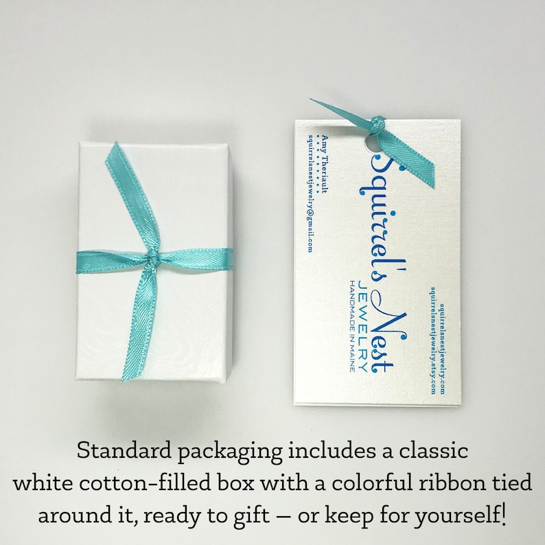 Puede incluir: Una caja blanca con una cinta azul claro atada alrededor. La caja est&aacute; sobre una superficie blanca. Tambi&eacute;n se muestra una tarjeta de presentaci&oacute;n de Squirrel's Nest Jewelry. La tarjeta es blanca con texto azul y dice "Squirrel's Nest Jewelry Handmade in Maine".