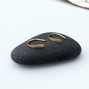 Puede incluir: Un par de peque&ntilde;os pendientes de aro de oro simples. Los pendientes est&aacute;n hechos de una fina pieza de metal plana que se dobla en forma de aro. Los aros tienen un di&aacute;metro de aproximadamente 1,25 cm.