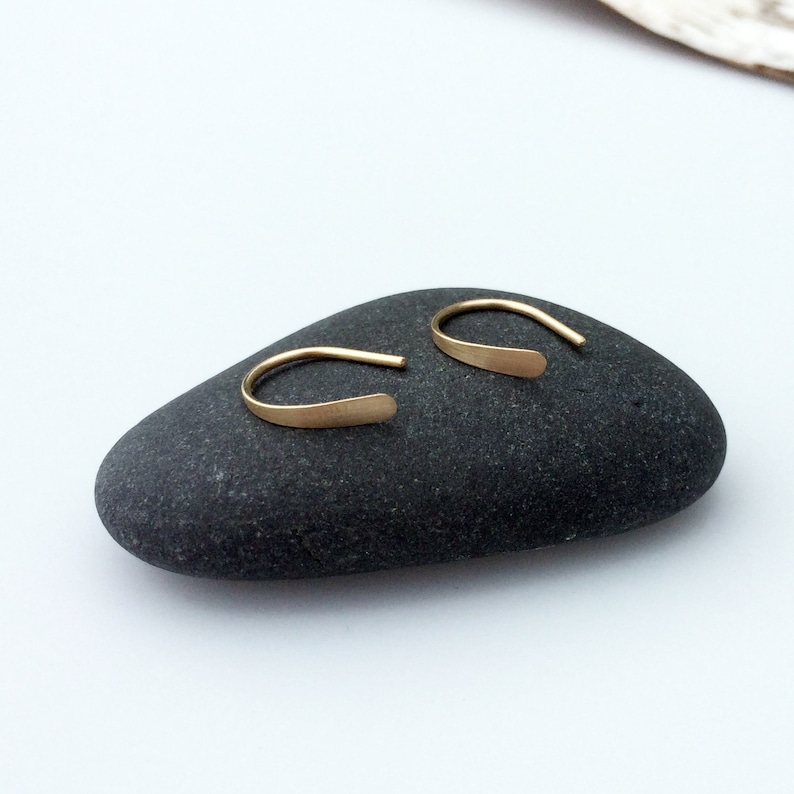 Puede incluir: Un par de peque&ntilde;os pendientes de aro de oro simples. Los pendientes est&aacute;n hechos de una fina pieza de metal plana que se dobla en forma de aro. Los aros tienen un di&aacute;metro de aproximadamente 1,25 cm.