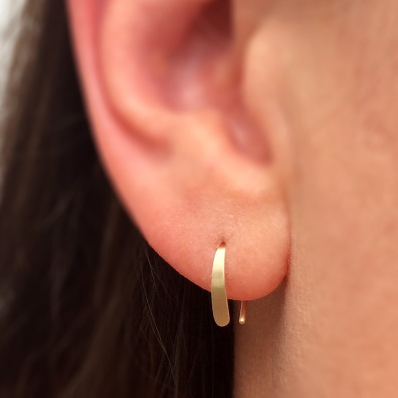 Puede incluir: Primer plano de una oreja con un peque&ntilde;o aro de oro fino. El arete es simple y discreto.