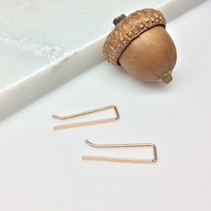 May include: A pair of rose gold ear cuffs. The cuffs are thin and have a simple, minimalist design.