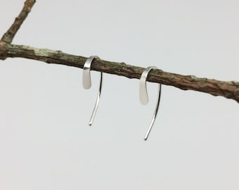 May include: A pair of silver hoop earrings with a simple, curved design. The earrings are hanging from a branch.