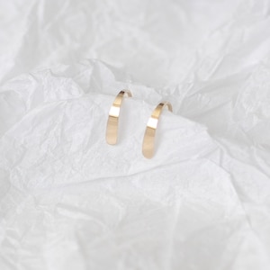 Puede incluir: Un par de pendientes de aro de oro. Los pendientes son simples y elegantes, con un acabado liso y pulido.