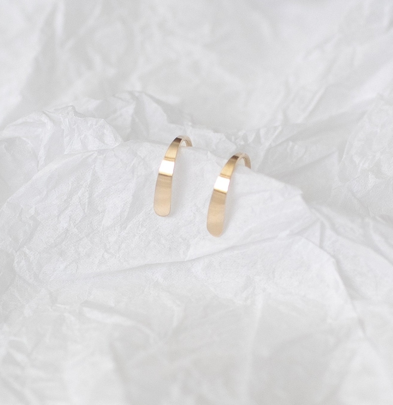 Puede incluir: Un par de pendientes de aro de oro. Los pendientes son simples y elegantes, con un acabado liso y pulido.