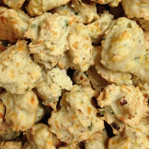 May include: A close-up of a bowl filled with small, golden brown, cheesy, and savory bites. The bites are irregular in shape and have a slightly crispy texture.