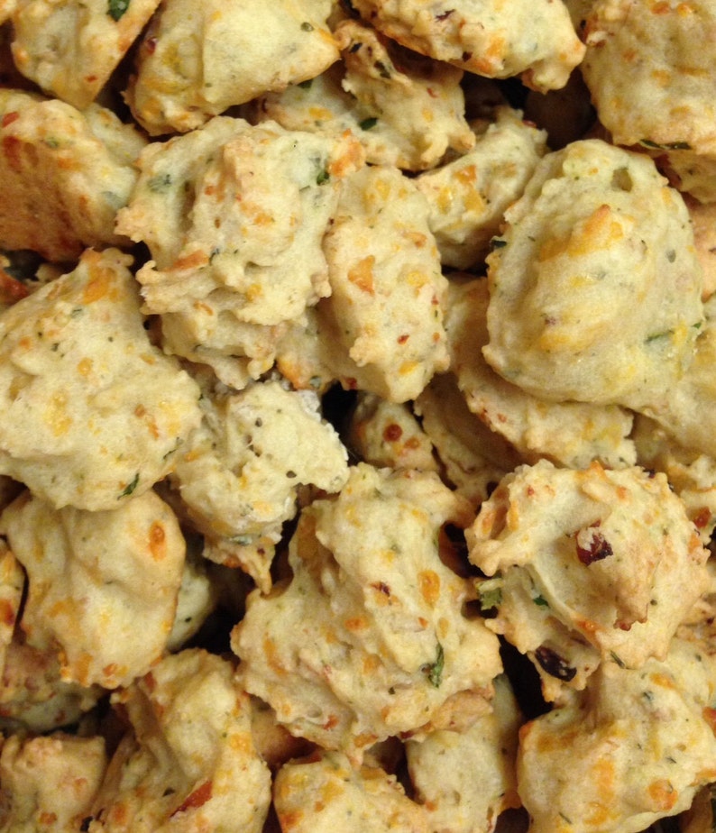 May include: A close-up of a bowl filled with small, golden brown, cheesy, and savory bites. The bites are irregular in shape and have a slightly crispy texture.