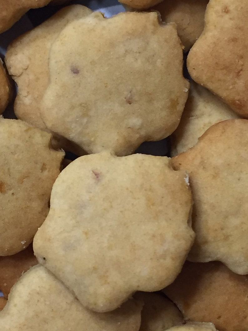 May include: A close-up of a pile of light brown, round, and slightly irregular shaped cookies. The cookies have a slightly rough texture and appear to be homemade.
