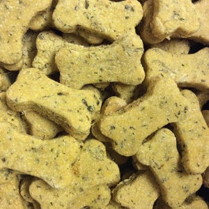 May include: A close-up of a pile of bone-shaped dog treats. The treats are a light brown color and have a slightly green tint. They are all in focus and appear to be made with natural ingredients.