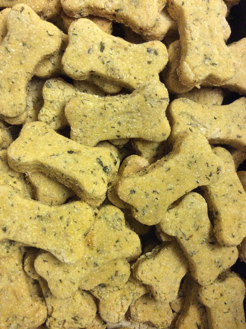 May include: A close-up of a pile of bone-shaped dog treats. The treats are a light brown color and have a slightly green tint. They are all in focus and appear to be made with natural ingredients.