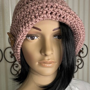 May include: A dusty rose crochet beret with a wooden button detail. The hat is made of a textured yarn and has a slightly slouchy fit. This handmade beret is a stylish accessory for any season.