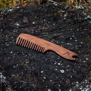 May include: A wooden comb with a brown handle and a natural wood finish. The comb has a small, triangular logo on the handle.