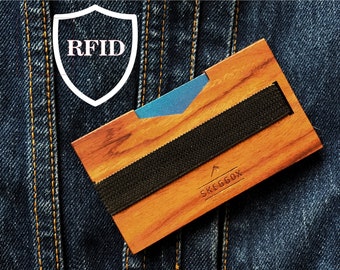May include: A wooden card holder with a black elastic band and the text "SKEGGÖX" printed on the front. The card holder is RFID blocking.