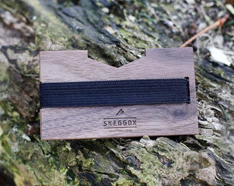 May include: A brown wooden wallet with a black elastic band and the text "SKEGGÖX ARTISANAL WOODNESS" engraved on the front.