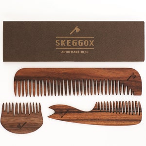 May include: Three wooden combs with a brown wood grain finish. The combs have a small axe logo engraved on them. The combs are arranged on a white background. The text "SKEGGOX ARTOFMANLINESS" is printed on a brown card behind the combs.