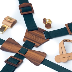 Puede incluir: Una pajarita de madera, tirantes, gemelos y una correa de cuero con hebilla. Los tirantes son verdes con hebillas de madera y la pajarita es de madera oscura. Los gemelos son dorados con una incrustación de madera. La correa de cuero es de color marrón claro con una hebilla.