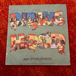 May include: A vintage children's book cover with a blue background and the title "Little Red Riding Hood and Other Stories" in large, colorful letters. The letters are formed by illustrations of the story characters.