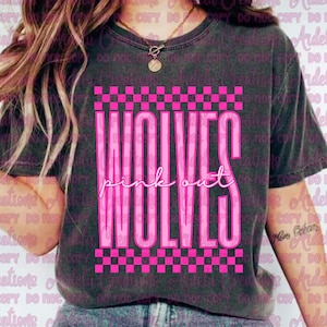 May include: Dark gray t-shirt with the words "WOLVES pink out" in bright pink. The text is framed by a pink and black checkered pattern. The shirt has a crew neck and short sleeves.