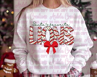 May include: White sweatshirt with the text "Santa's favorite LIONS" in red and green. The word "LIONS" has a candy cane design with a red bow. The sweatshirt is paired with red and black plaid pajama pants.