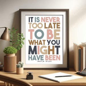 May include: A framed print with the quote "IT IS NEVER TOO LATE TO BE WHAT YOU MIGHT HAVE BEEN" by George Eliot. The text is in various colors, including pink, brown, and blue. The frame is dark brown, and the print is displayed on a wooden desk.