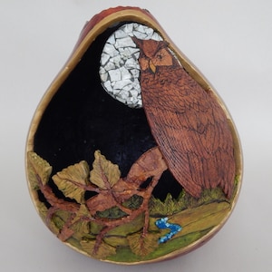 May include: A handcrafted, teardrop-shaped wooden bowl featuring a detailed owl perched against a night sky with a mosaic moon. The bowl's interior is black, with a painted landscape and foliage at the base. The owl is brown with intricate feather details.