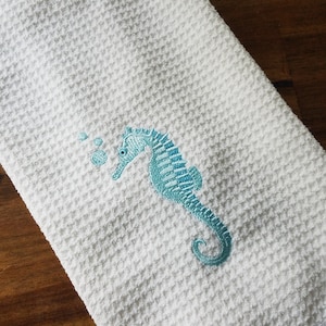 May include: White waffle weave kitchen towel with a blue embroidered seahorse and bubbles.