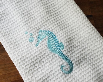 May include: White waffle weave kitchen towel with a blue embroidered seahorse and bubbles.