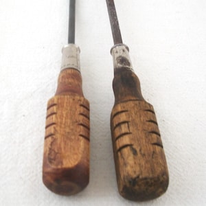 May include: Two vintage screwdrivers with wooden handles. The handles are a warm brown color with carved grooves for grip. The metal shafts are dark and show signs of age and use. The screwdrivers are likely antique tools.
